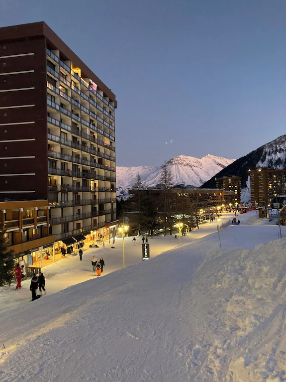 Front de neige du Corbier au crépuscule, commerces éclairés au pied de la résidence